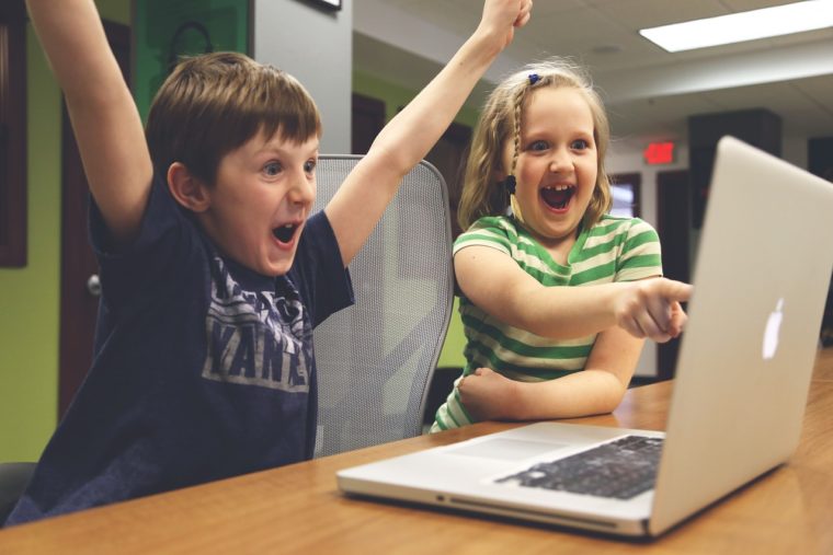 Hooray for accessibility! A boy and girl are looking at a laptop and cheering. The boy has his hands in the air, and the girl is pointing at the screen.