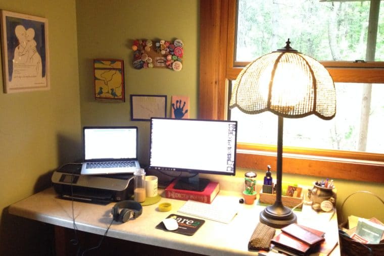 A Cornershop Creative employee's office setup. Desk, laptop on top of printer, second monitor, and old fashioned lamp