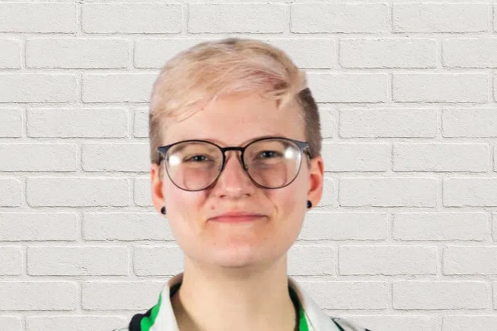 A person with short blonde hair wearing glasses.